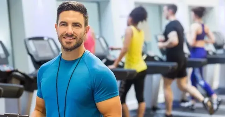 Man smiling in gym with people running on treadmills in the background