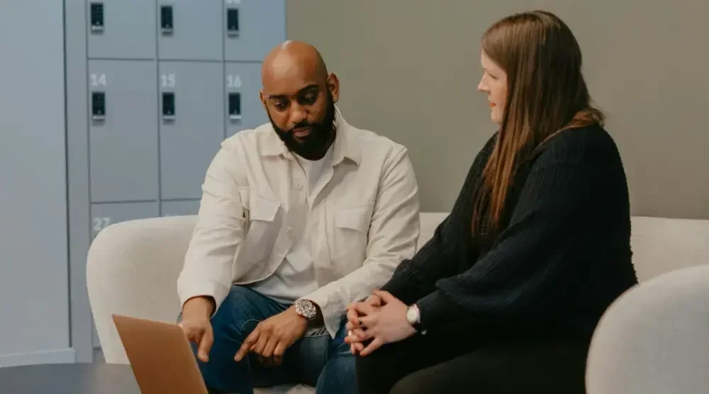 A man and a woman sit on a couch and talk as the man points at a laptop. You may want to hire a business consultant for expert help in facing challenges such as a company transition or stagnant growth. 