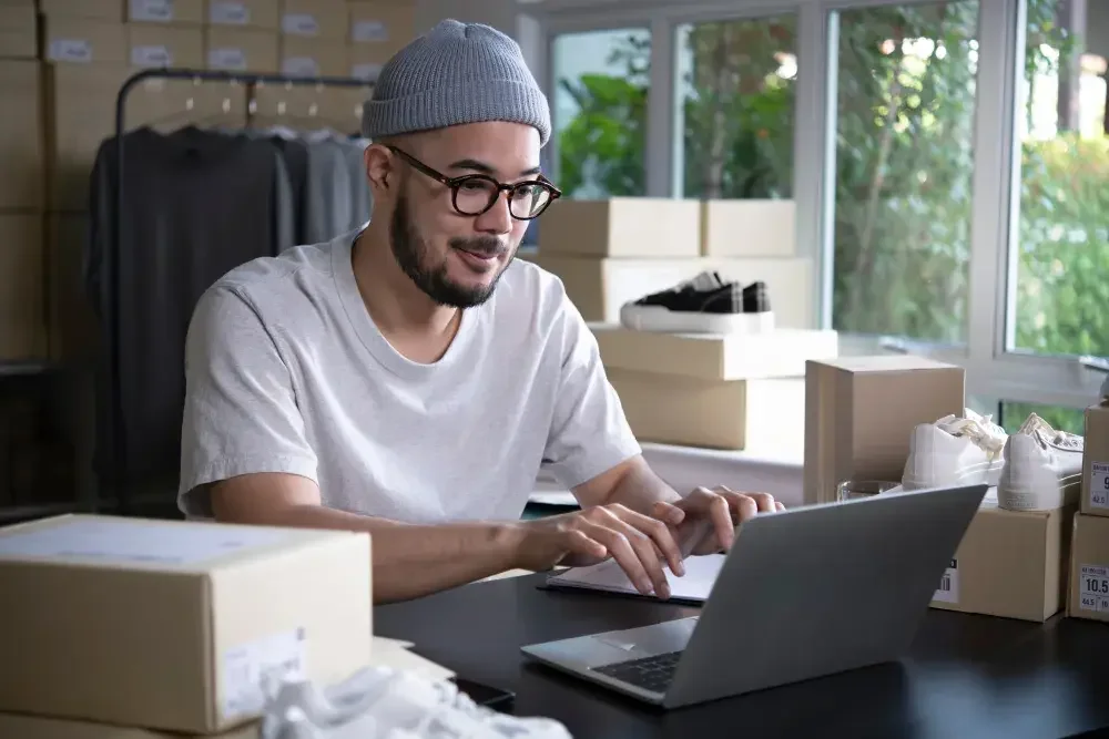 A Wyoming man in a beanie checks orders on his laptop for his clothing line. Wyoming has relatively low filing fees for both formation and annual maintenance. 