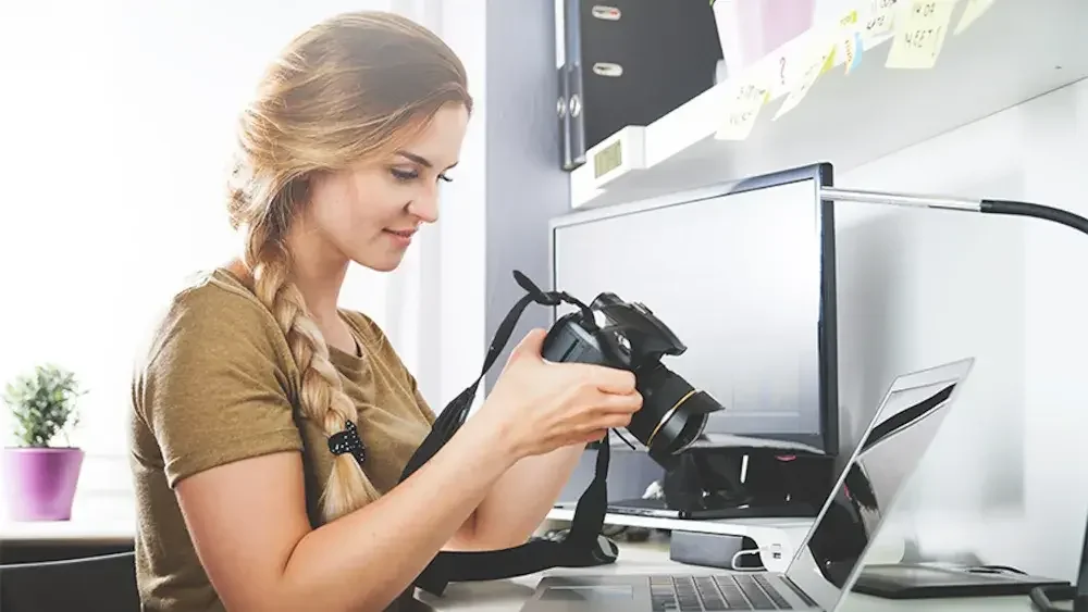 A photographer inspects her camera while seated in front of her computer. A registered LLC makes it possible for you to obtain a business bank account and more.