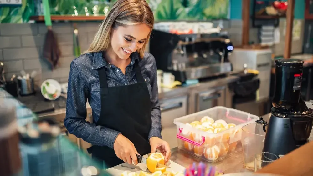 A woman wearing an apron slices lemons on a counter in her smoothie shop. To obtain a Florida business license, you'll need to supply your LLC name, EIN, address, and contact information.