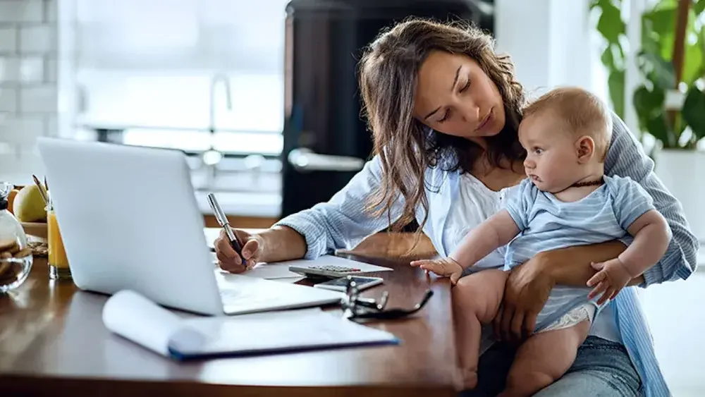 A business owner and mother holds her baby while doing calculations on a desk as she registers for an Employer Identification Number.