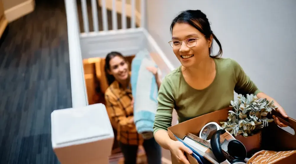 Two women climb the stairs with household items. A joint tenancy can be created with spouses, family, friends, or domestic partners.