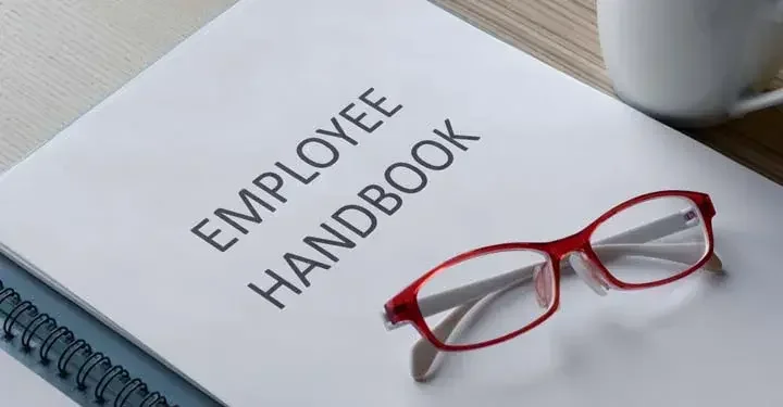 Stack of papers labeled "Employee Handbook" with a pair of glasses sitting on top