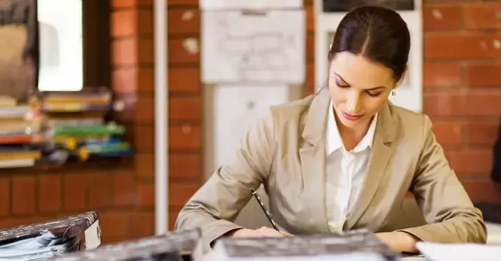 woman in brown jacket writing in notebook 