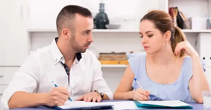 Man and woman sadly looking at each other while they hold ballpoint pens over forms