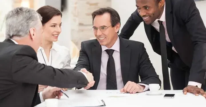 Four businesspeople make an agreement above documents on white desk as two people shake hands