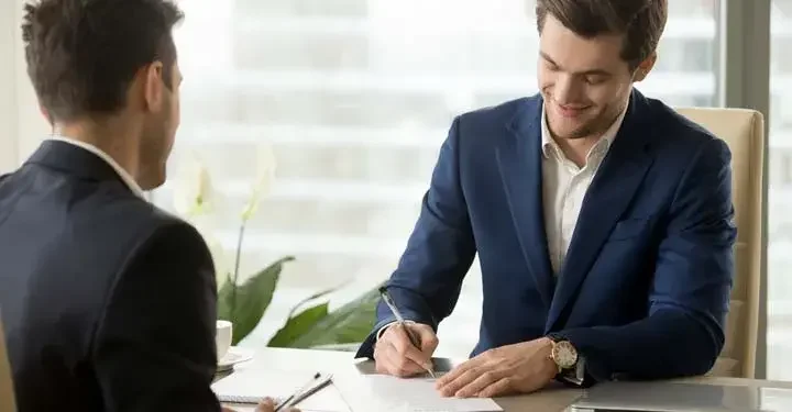 Businessman signing documents as a coworker watches from across the desk