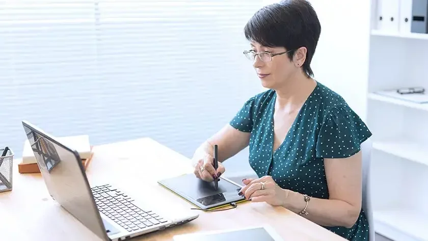 woman-working-at-desk-on-laptop-using-stylus