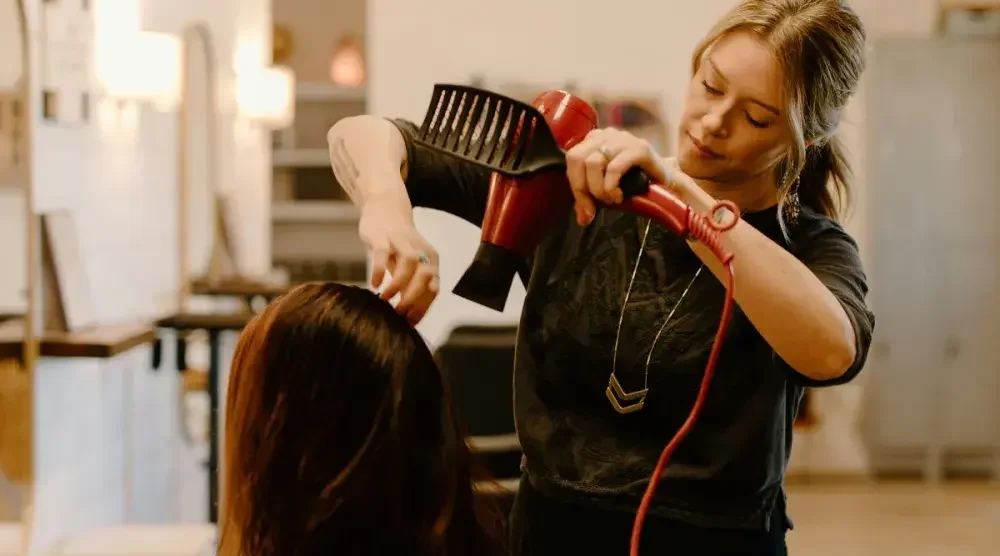 A hairstylist blow-dries her client's hair in a salon.