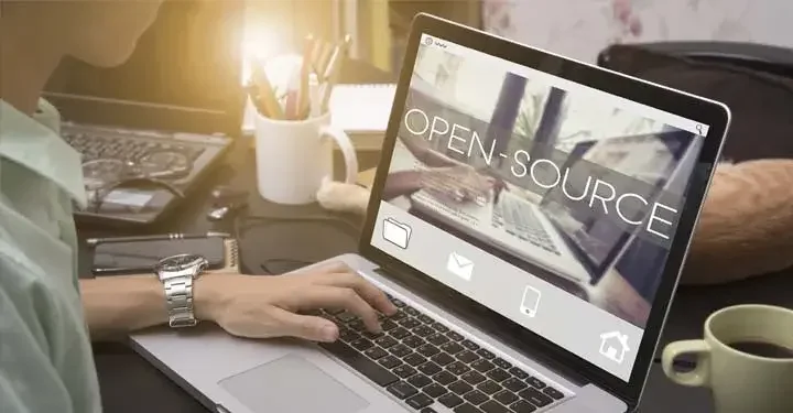 Laptop on cluttered desk with inspiring warm backlight with large text reading "open-source" on the screen