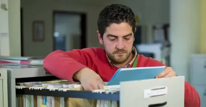 Man standing at an open filing cabinet pulling out a folder