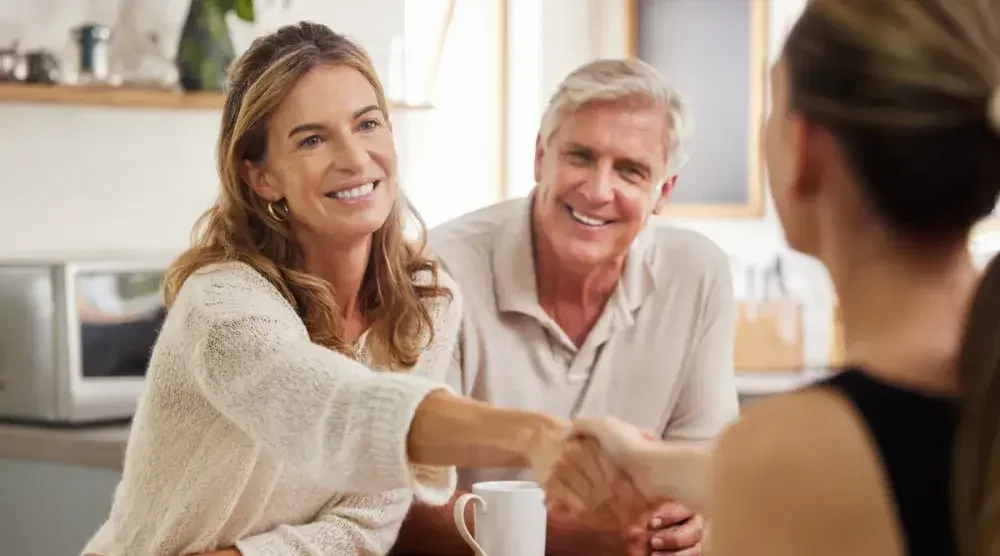 A man and a woman smile as the woman shakes hands with a woman across the table. Marriage, divorce, or personal preference are common reasons to change your legal name in Washington.