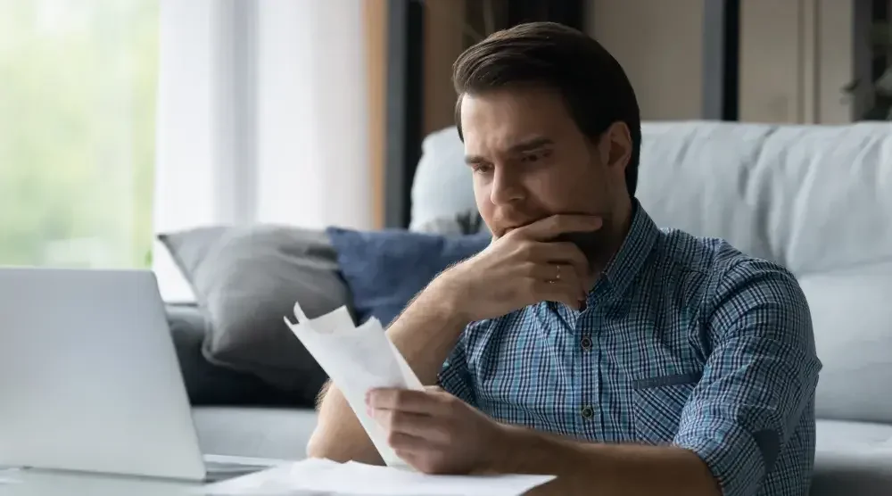 A man sits at a desk in front of a laptop looking through business documents and considering filing for bankruptcy