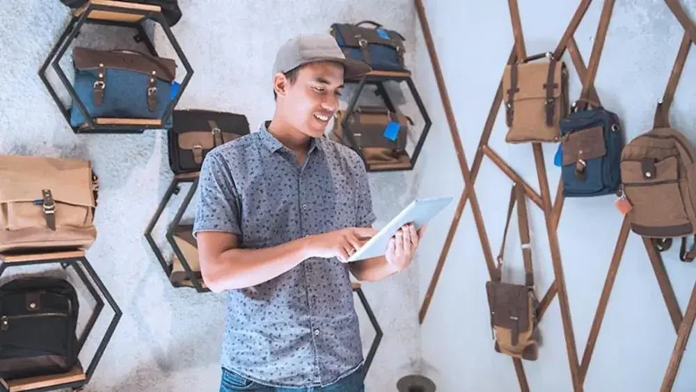 A man checks online orders for bespoke backpacks at his shop.