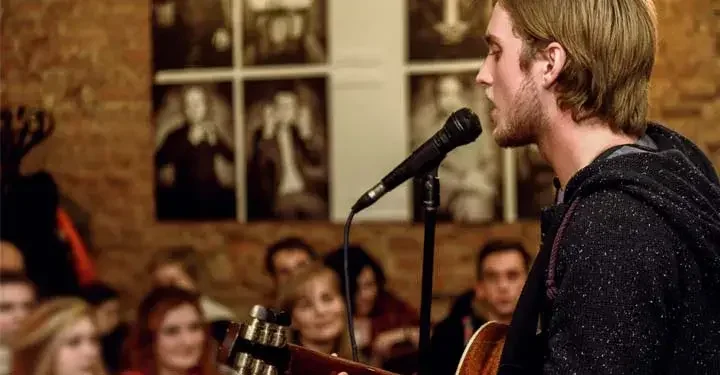 Man standing at microphone, playing guitar for an audience