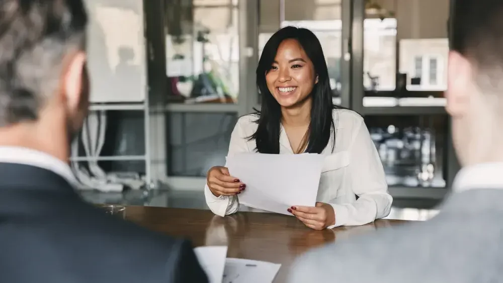 A woman behind a desk explains to clients the difference between FUTA and SUTA payroll taxes.