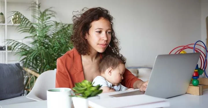 Woman holding baby working at a laptop