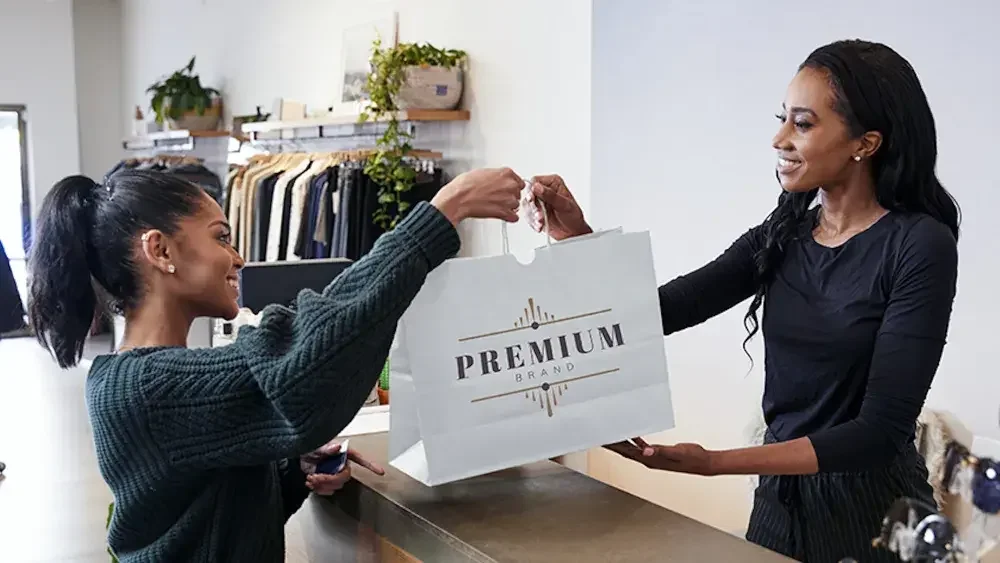 A woman behind a counter at a clothing shop hands a bag to a customer. Florida LLCs are required to file their annual report online between Jan. 1 and May 1 each year. 