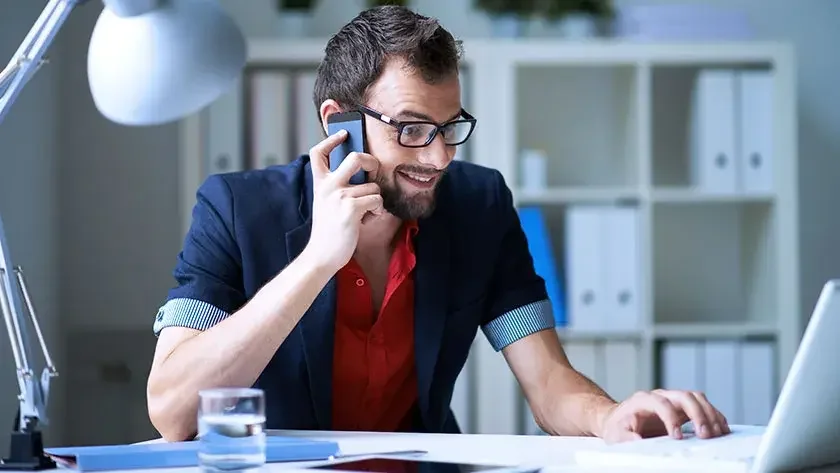 man-smiles-talking-on-phone-looking-at-laptop