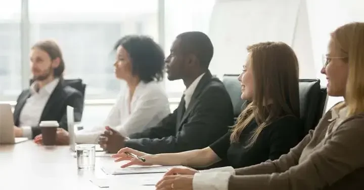 Businesspeople smiling contentedly at roundtable with variety of drinks and pens and papers on table in front of large window