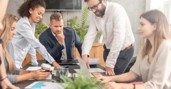 Business people sitting and standing around a table collaborating