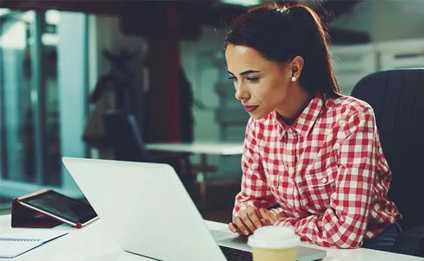 A woman sitting at a desk and researching how to change a name on a birth certificate on her laptop