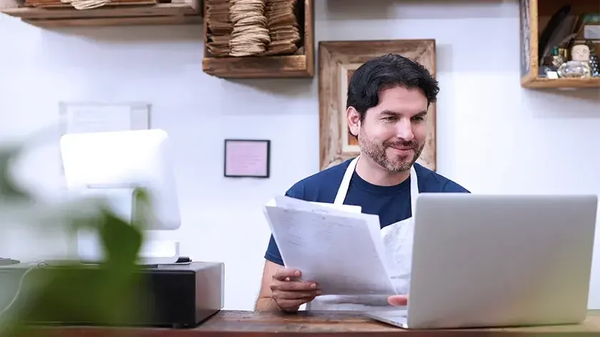 A man seated at a counter looks at his open laptop. This article explains what to know before you open a business in a bear market.