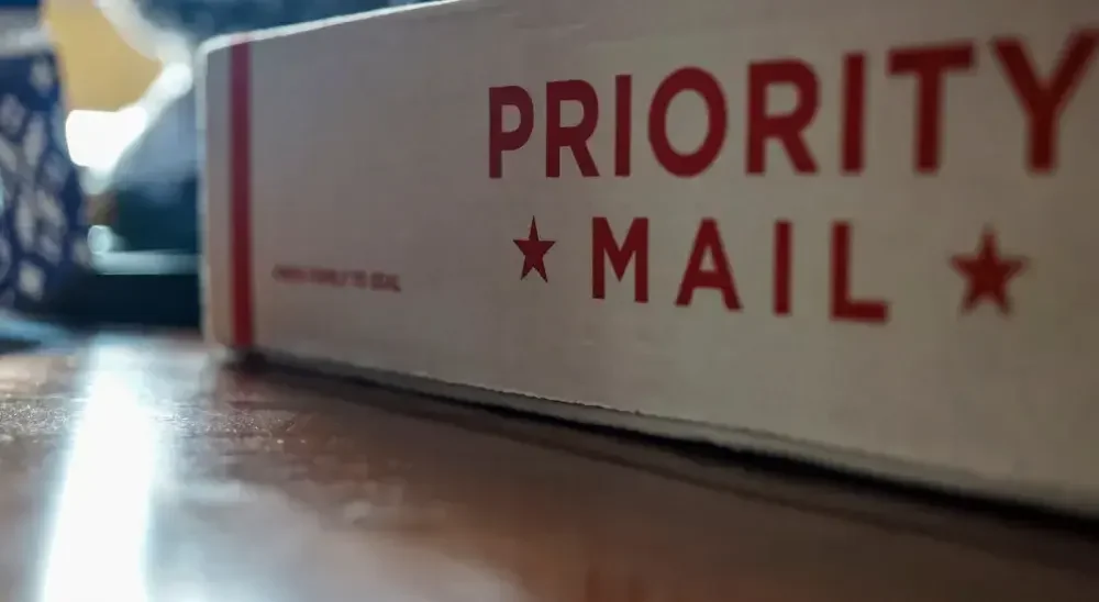 A white U.S. Postal Service box with red letters reads, "Priority Mail."