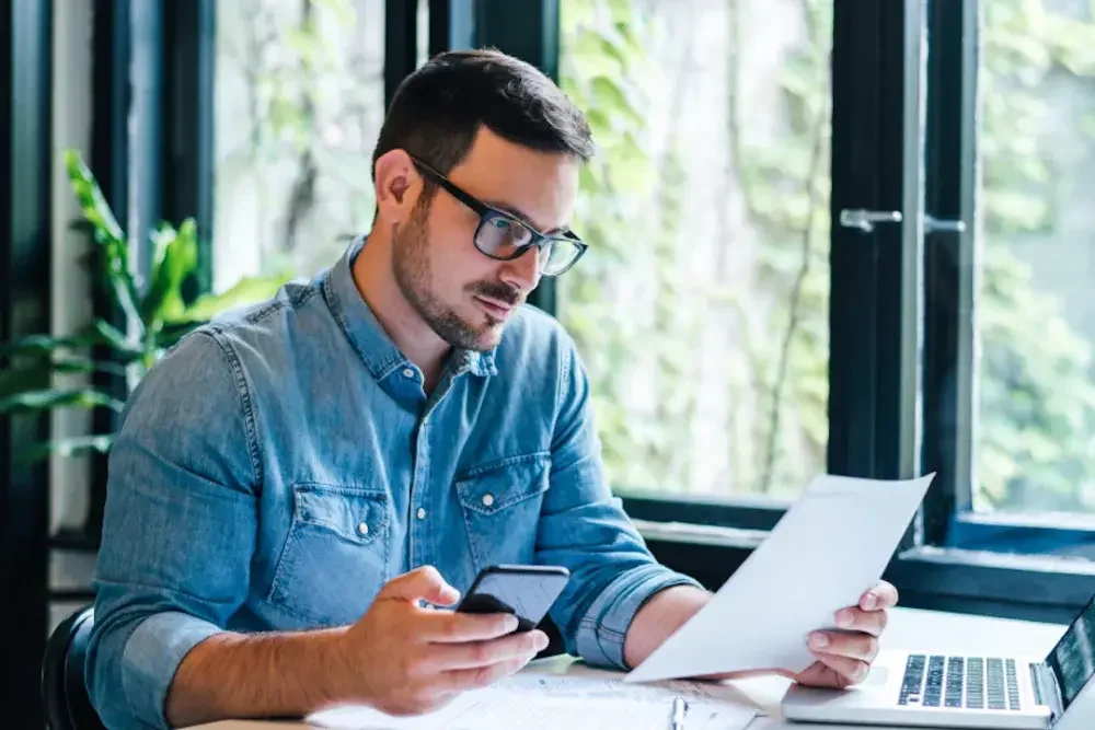 A business owner checks his paperwork against his cell phone to file as an S corporation.