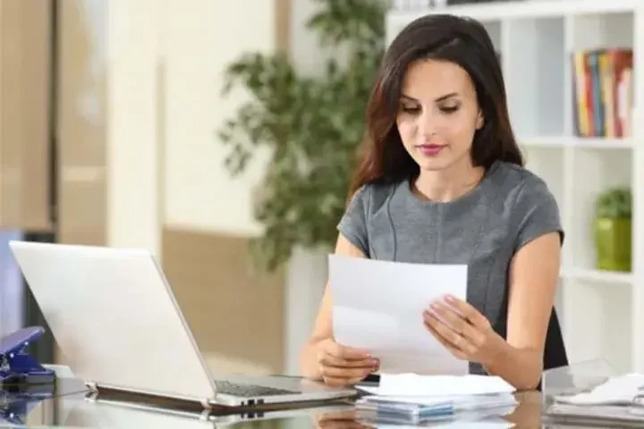 Woman sitting at desk with open laptop looking at paperwork