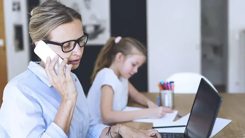 woman-working-at-home-on-laptop-next-to-child while she colors 