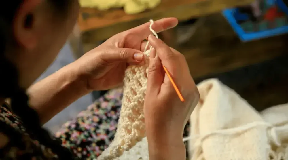 Looking over the shoulder at a woman's hands as she crochets a blanket.