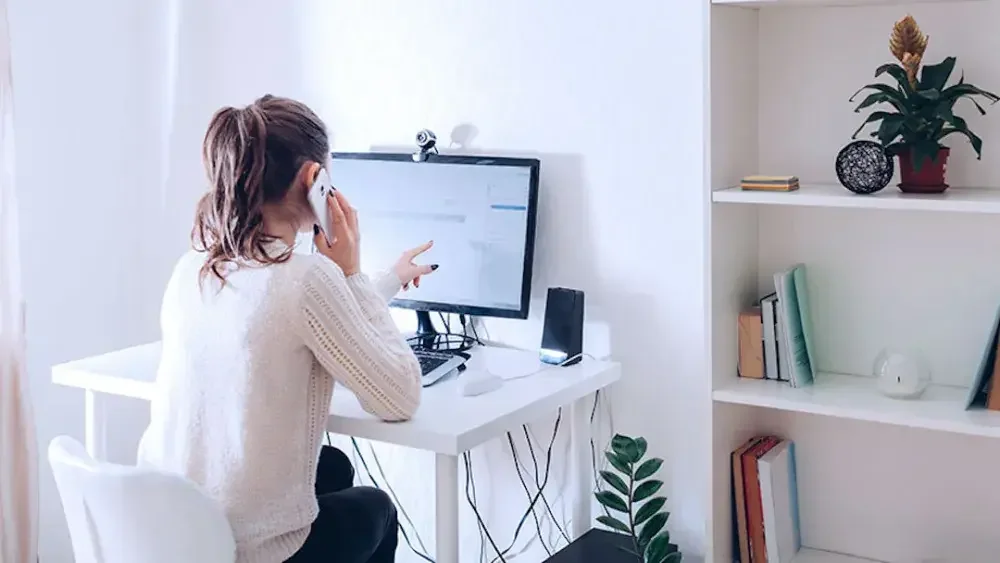 A business owner on her cell phone points to her desktop computer screen as she reads about complications that can arise when filing your LLC in a state that's not where your income property is located.