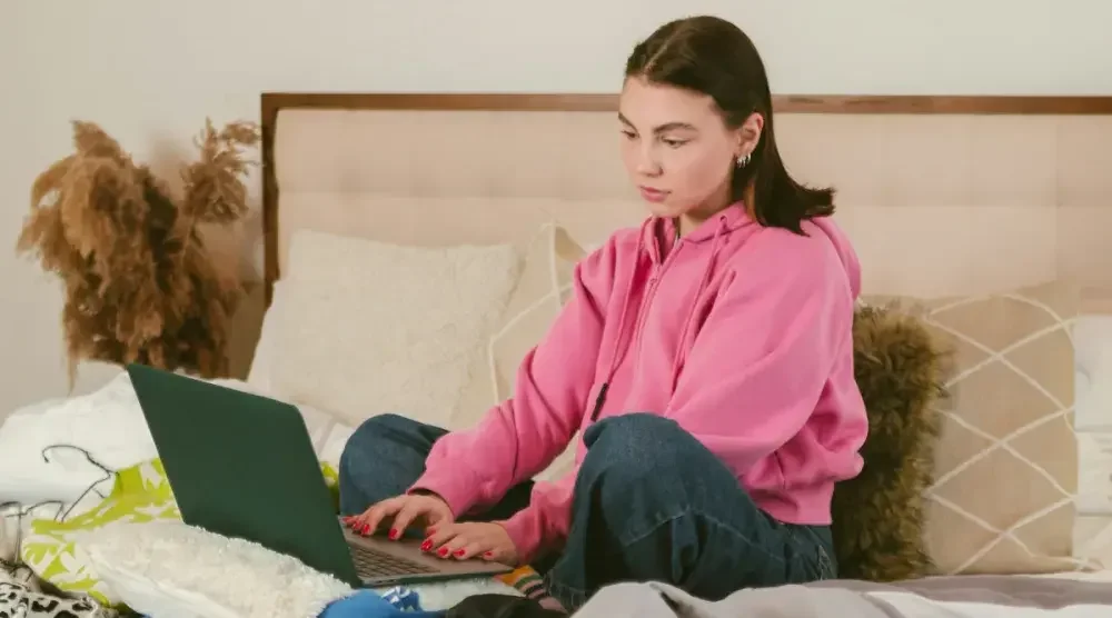 A young woman sitting on her bed and researching how to get a legal name change in California on her laptop