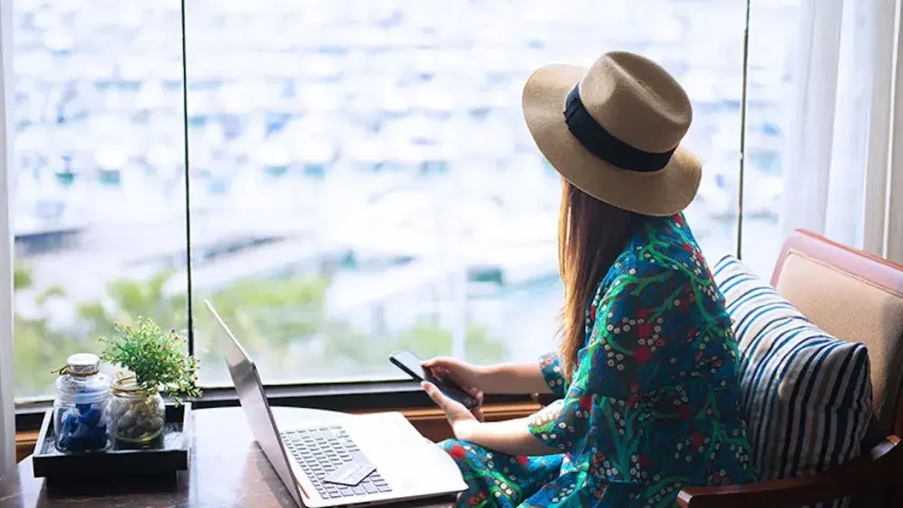 A woman in a cafe holds her phone and looks out a window after filing her annual report online. To maintain LLC status with the state, she must file an annual report and ensure that all necessary business licenses are up-to-date. 