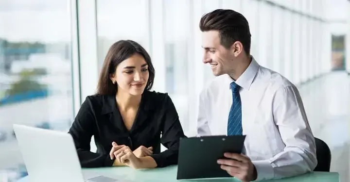 Coworkers with open laptop looking at a clipboard