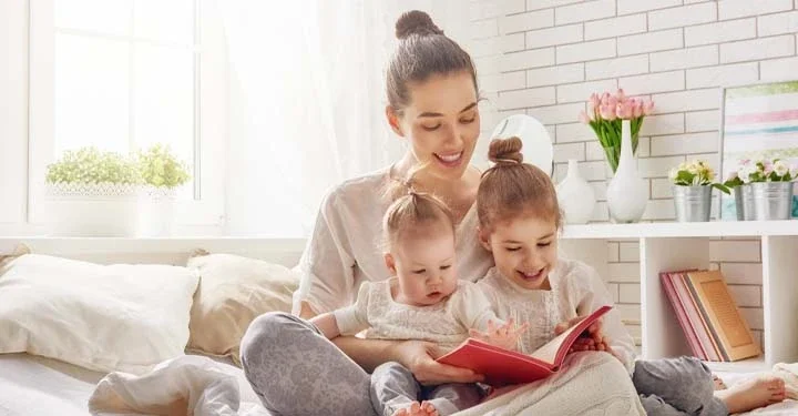 Woman holding two young children reading a book