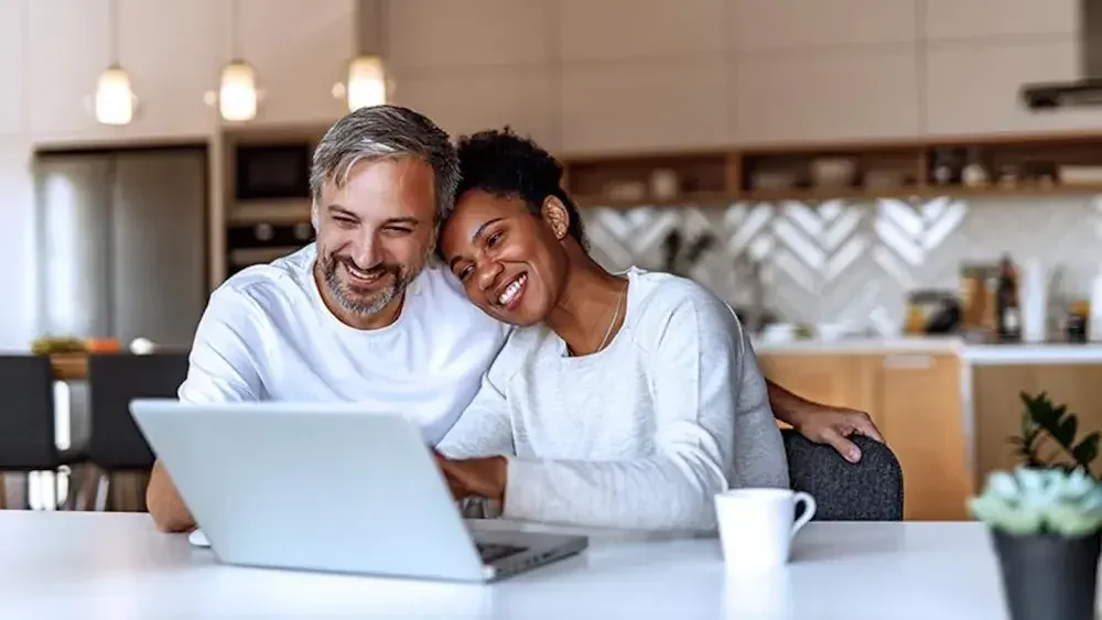 A man and a woman sit at their kitchen counter looking at an open laptop as they complete their articles of organization. This document establishes your LLC by laying out basic information about it.