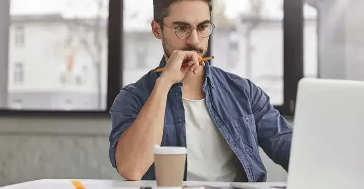 Man holding pencil working on his laptop