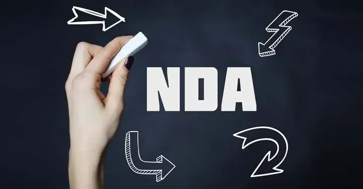 Hand holding a piece of chalk on a black backdrop with white letters spelling "N.D.A."