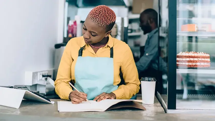 woman in bakery writing in ledger 