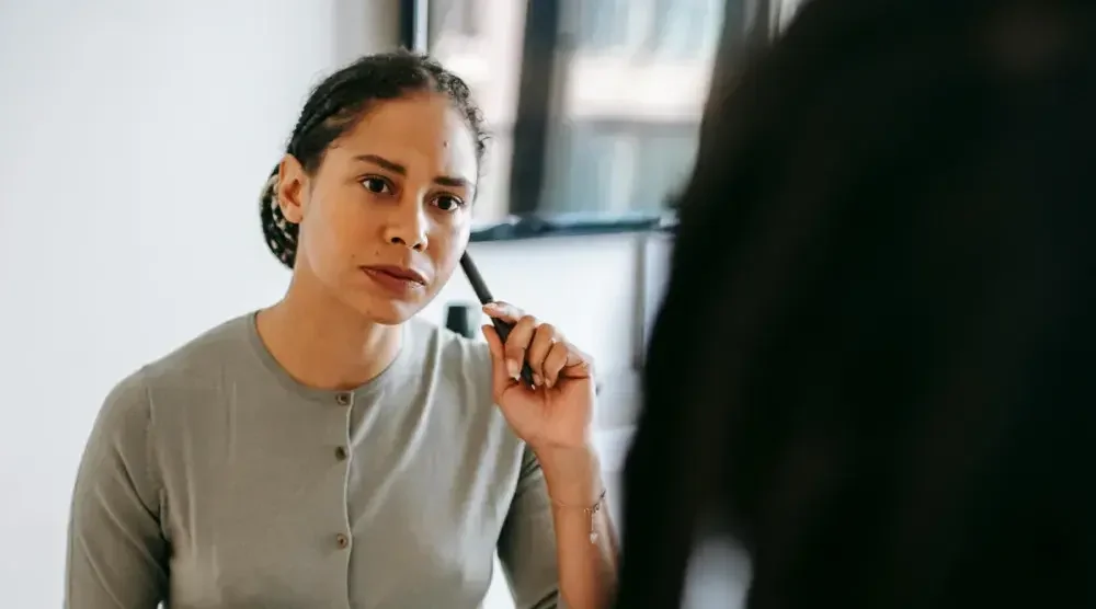 A woman in a cardigan holds a pen up to her face as she contemplates no-fault divorce.