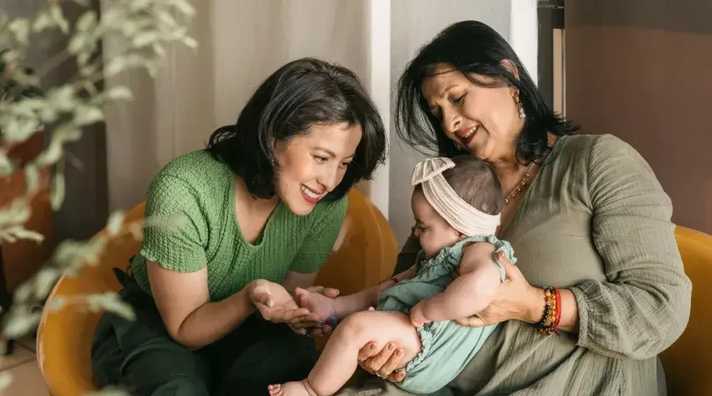 Two women sitting on yellow chairs playing with a baby and discussing starting an estate plan