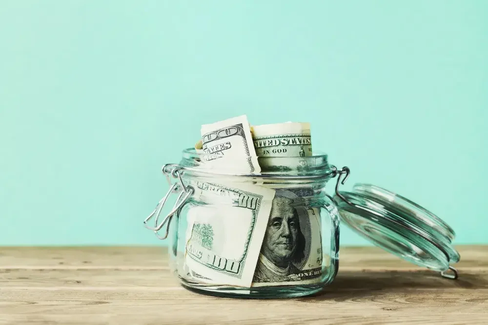 A mason jar of $100 bills sits on a counter. tax professionals can provide valuable advice on the tax implications of forming an LLC in a specific state