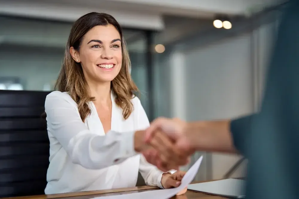 A woman seated at a desk shakes hands with her new registered agent in Illinois.