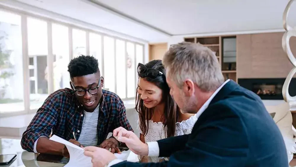 A man and woman sit on one side of a desk examining living trust documents while an estate planning attorney sits opposite them and explains.