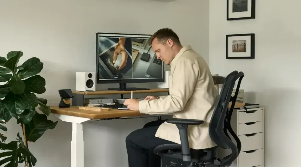 A man sits at his desk in a light-filled office and fills out a form on his tablet.