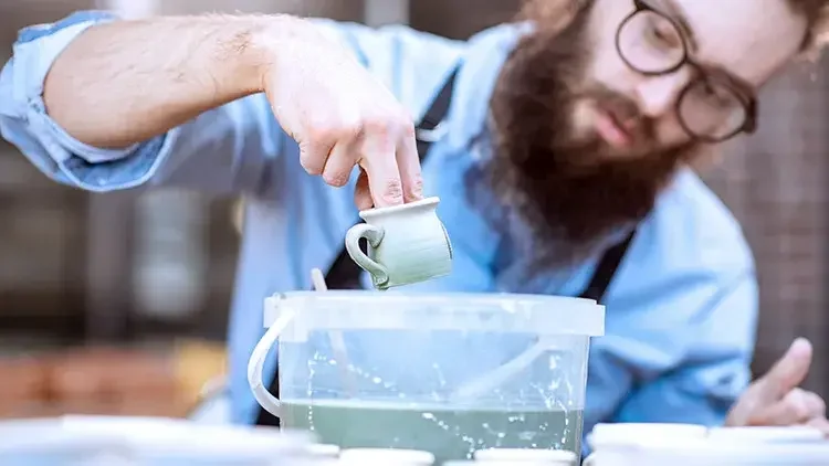 Man dipping pottery in glaze