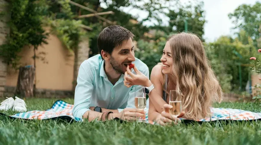 A woman feeds her fiance a berry as they lie on a blanket outdoors and sip champagne. Deciding whether a prenup is appropriate for you and your spouse-to-be is an intensely personal process